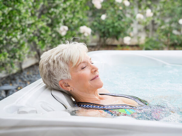 An older woman relaxes and enjoys a bubbly soak in a luxurious Caldera Spa hot tub, helping to fight a common cold with the therapeutic benefits of hydrotherapy.