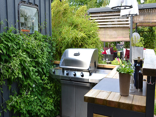 Outdoor lounging area with a grill. The area has comfortable seating, a grill, and a fire pit. The background is a lush green lawn.