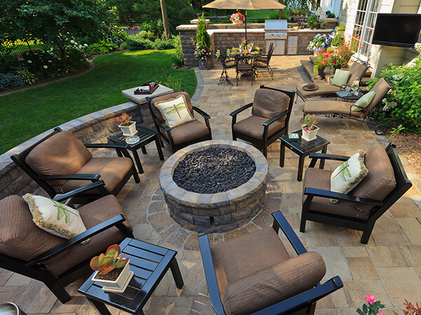 An outdoor living area with a firepit. The firepit is surrounded by comfortable seating and a lush green lawn. The image is a great example of backyard design ideas that incorporate firepits.