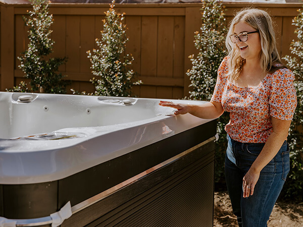 A smiling Caldera Spas marketing team member stands proudly next to a Utopia Series Geneva spa with a Java cabinet and Arctic White shell. 