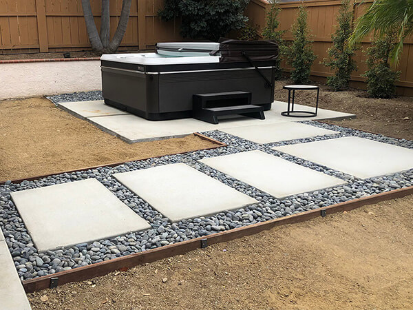 A modern backyard oasis featuring a sleek hot tub surrounded by a beautifully designed concrete paver patio. The pavers create a stylish and functional pathway.