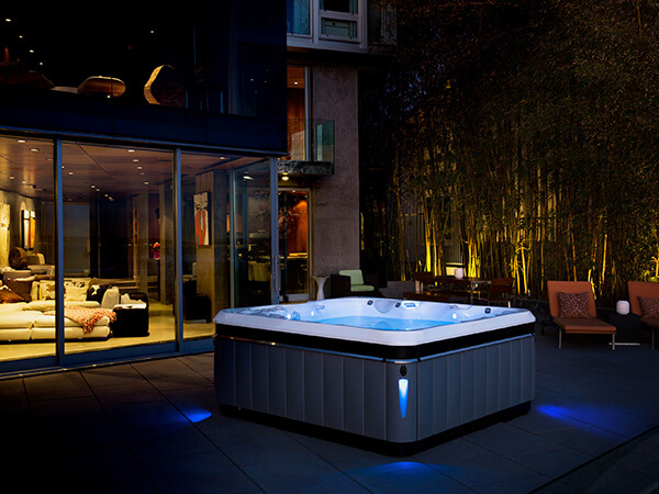 A modern hot tub sits on a patio, illuminated by warm lights.