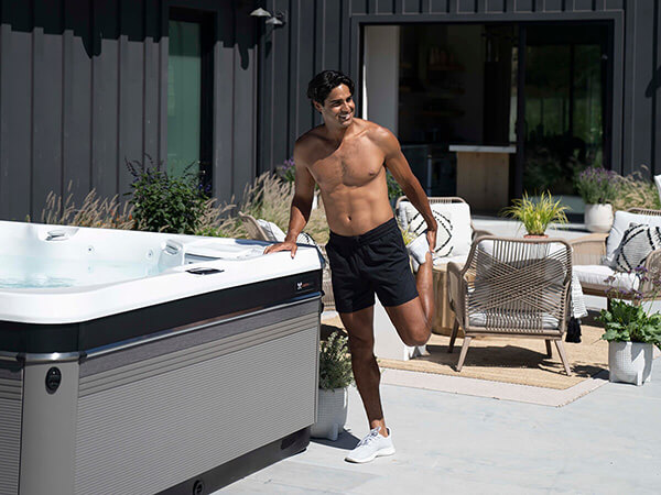 A man stretches besides a Caldera Spa enjoying the benefits of improved range of motion provided by hot tub usage.