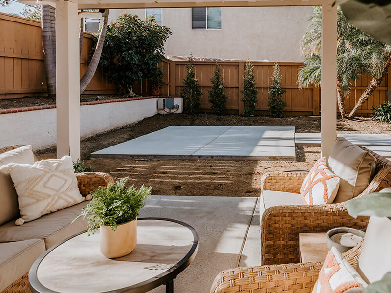 Outdoor patio with wicker furniture overlooking a hot tub concrete pad in a backyard.